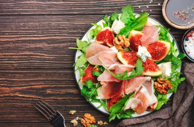 Jamonlu incir salatası, mavi peynir, ceviz, ahşap mutfak masasında roka, üst manzara, kopyalama alanı.