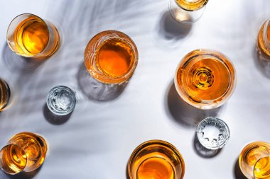 Sert içkiler, içkiler ve bardaklarda damıtılıyor: konyak, grappa, votka, viski ve çeşitli içecekler. Sert ışık ve sert gölgelerle beyaz arkaplan