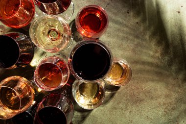 Kırmızı, beyaz ve gül şarapları yeşil arka planda çeşitli bardaklarda, üst manzara. Şarap barı, dükkan, şaraphane, şarap tatma konsepti. Sert ışık ve sert bitki gölgeleri