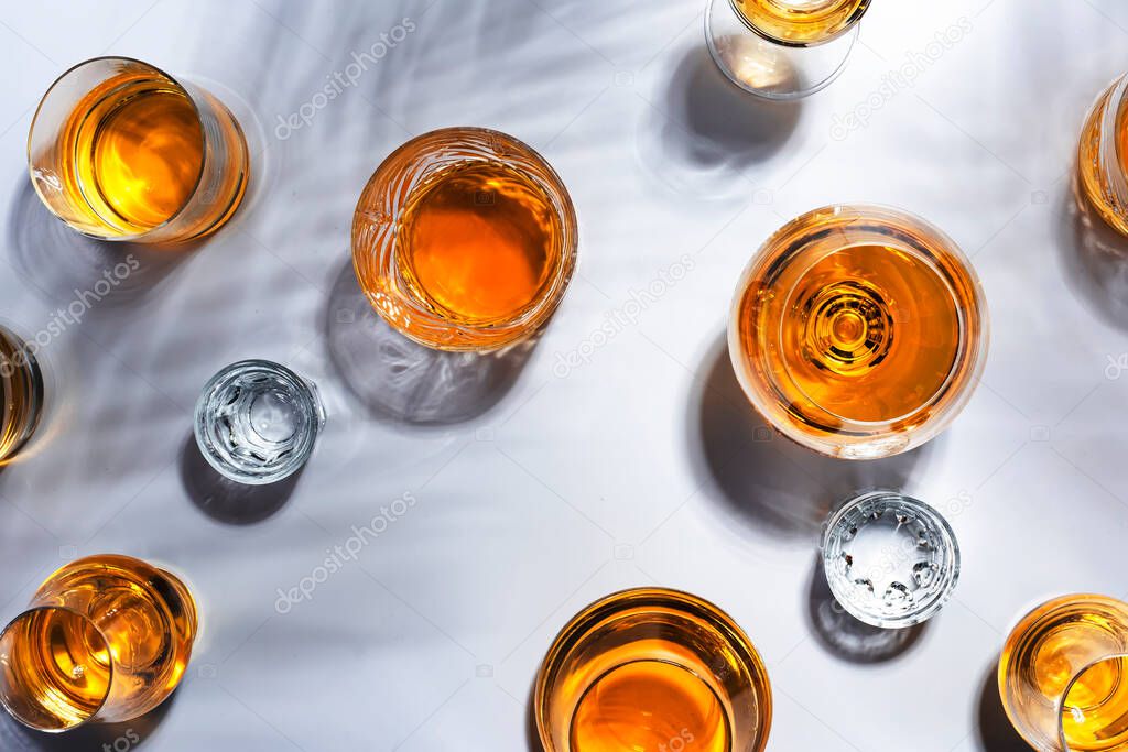 Strong drinks, spirits and distillates in glasses: cognac, grappa, vodka, whiskey and other in assortment. White background with hard light and harsh shadows