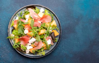 Kavunlu yaz salatası, prosciutto, beyaz peynir ve roka mavi masa arka planında, üst manzara, kopyalama alanı