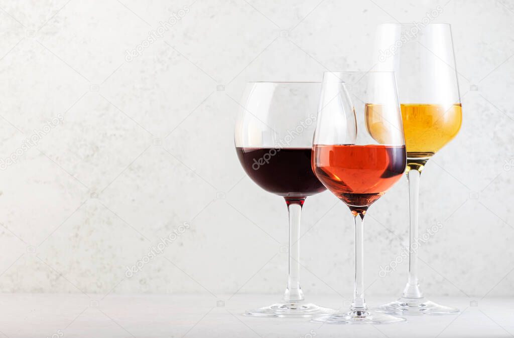 Red, rose and white wine glasses set on gray table background. Wine tasting. Hard light and harsh shadows