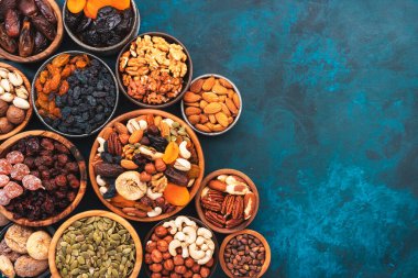 Çeşit çeşit fındık ve kurutulmuş meyve. Kuru kayısılar, incirler, kuru üzümler, cevizler, bademler ve diğerleri. Mavi tablo arkaplanı, üst görünüm, kopyalama alanı