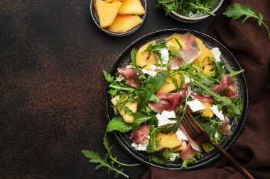Kavunlu yaz salatası, jamon, beyaz peynir ve roka kahverengi masa arkasında, üst görünüm, kopyalama alanı