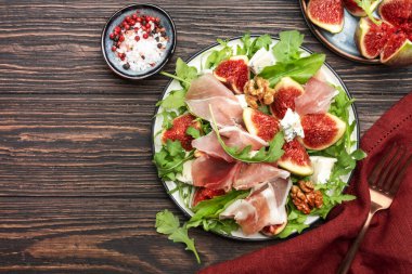 Jamonlu incir salatası, mavi peynir, ceviz, ahşap mutfak masasında roka, üst manzara, kopyalama alanı.