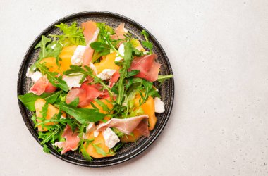 Kavun salatası kavun, prosciutto, yumuşak peynir ve roka beyaz masa arkasında, üst görünümde, kopyalama alanı