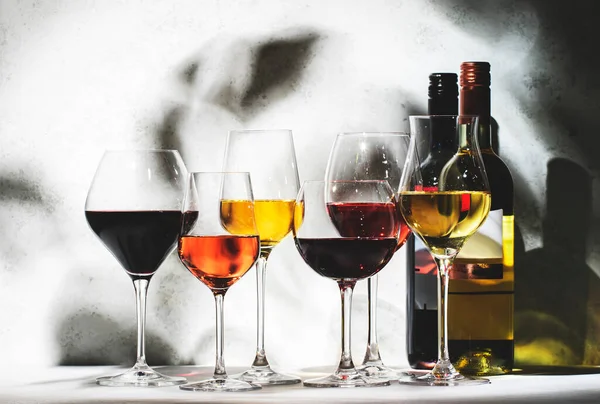 Red, rose and white wine glasses set on gray table background. Wine tasting. Hard light and harsh shadows