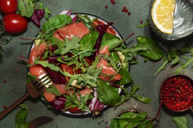 Pancar yapraklı taze somon salatası, domates, keto ve düşük karbonhidrat diyeti için limon ve zeytin yağı sosu. Paslı yeşil arkaplan, sert ışık, üst görünüm, kopyalama alanı