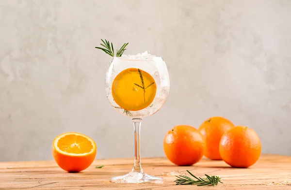 Gin tonic cocktail long drink with dry gin, bitter tonic, orange, rosemary and ice. Wooden table background with copy space