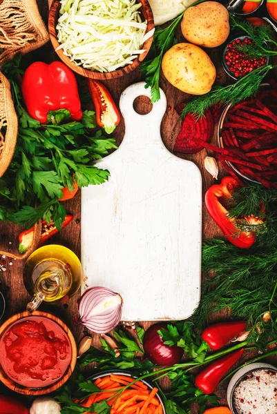 Sağlıklı yemek pişirmek için çeşitli pişmemiş sebzeler, otlar ve baharatlar ve kırsal mutfak ahşap masasında beyaz kesim tahtaları, üst manzara. Vejetaryen lahanası, pancar kökü, domates çorbası. Vejetaryen, dengeli, diyet yemekleri. 