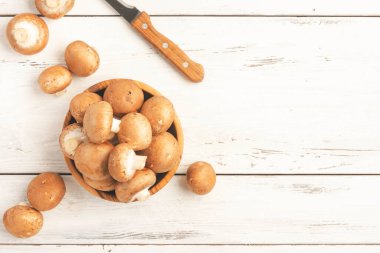 Çiğ kahverengi şampiyon mantarları ahşap zeytin kasesinde, eski beyaz mutfak masası, üst manzara, negatif uzay