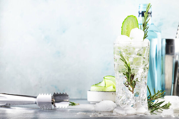 Джин тоник с огурцом, алкогольный коктейль с сухим джином, розмарином, тоником, свежим огурцом и кубиками льда. Серый фон, штрих-инструменты, пространство для копирования