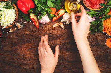 Taze vejetaryen malzemeler, sebzeler, baharatlar, saglikli yemek icin saglikli otlar saglikli ahşap mutfak masasinda kesme tahtasiyla. Kadın eli yağ şişesini alır. Diyet, temizlik, konfor yemek pişirme konsepti