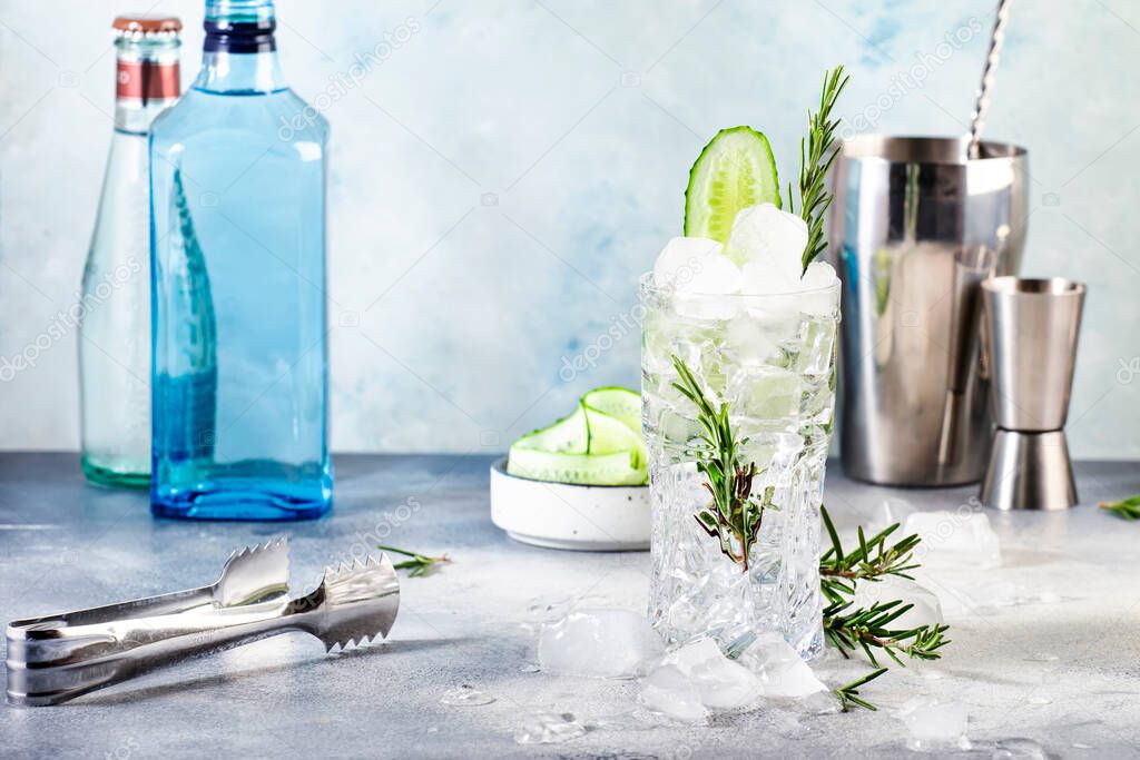 Gin tonic with cucumber, alcoholic cocktail drink with dry gin, rosemary, tonic, fresh cucumber and ice cubes. Gray background, bar tools, copy space