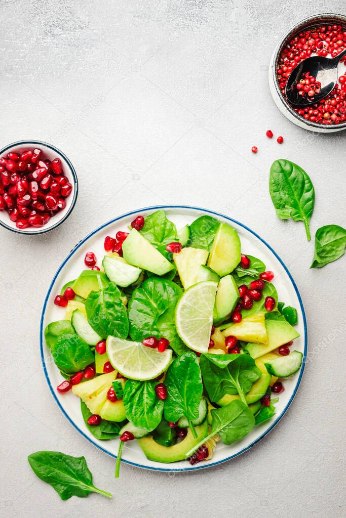 Vegan vegetarian salad with pineapple, spinach, avocado and pomegranate, gray stone kitchen table, top view. Healthy eating, clean food, diet, weight loss concept