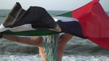 Deniz sahilinde mayolu çekici bir kadın, BAE bayrağıyla, yakın plan.