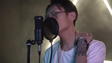 Kayıt stüdyosunda mikrofona şarkı söyleyen genç bir Asyalı. Asyalı şarkıcı veya müzisyen