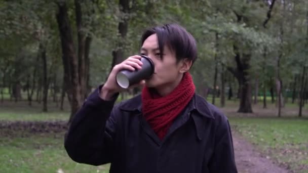 Junger asiatischer Mann beim Kaffeetrinken im Herbstpark. Herbst, Porträt eines attraktiven Mannes im Freien — Stockvideo