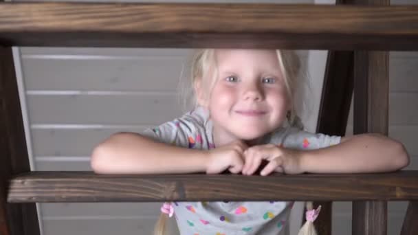Glückliches Mädchen auf den Stufen einer hölzernen Leiter in einem Landhaus — Stockvideo
