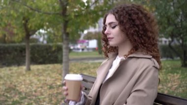 Güz, genç ve güzel bir kadın kahve içer ya da parkta bir bankta sıcak bir içki içer.