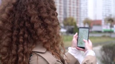 Bir kadın elinde şehrin elektronik haritası olan bir akıllı telefon tutuyor. Biri telefonunda navigatör kullanıyor.