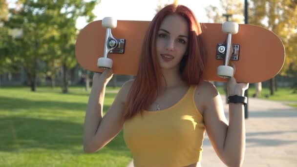 Портрет молодой привлекательной женщины со скейтбордом в парке на открытом воздухе — стоковое видео