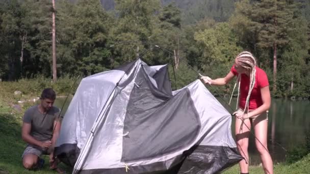 Heureux couple de randonneurs lors d'une randonnée érigé une tente au bord du lac dans la forêt — Video