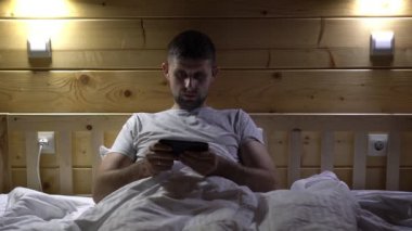 Erkek bir oyuncu akşamları yatakta telefonla oyun oynar. Adam akıllı telefonuyla oynuyor. Video oyunlarına kumar bağımlılığı