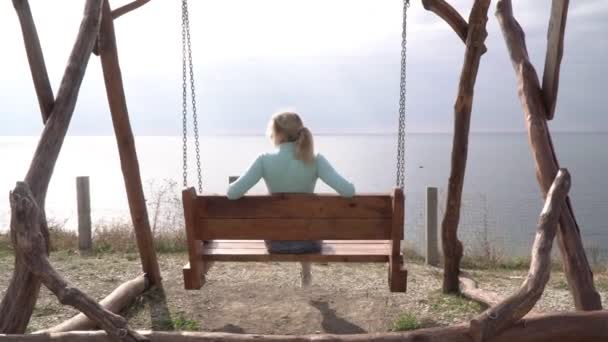 Jovem em um balanço com vista para o mar. Mulher bonita balançando em um balanço contra o fundo do mar — Vídeo de Stock