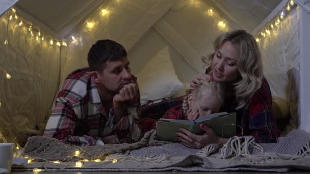 クリスマス、親は就寝前に子供におとぎ話を読みます。幸せな家族は新年の前に本を読む — ストック動画