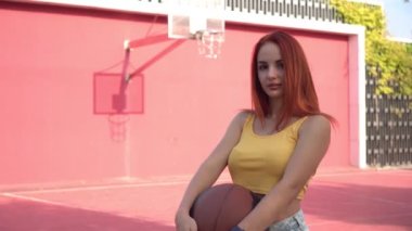 Açık havada basketbol oynayan sportif seksi bayan öğrenci. Sokak basketbol sahasındaki genç kızıl saçlı kadın. Modern spor gençliği