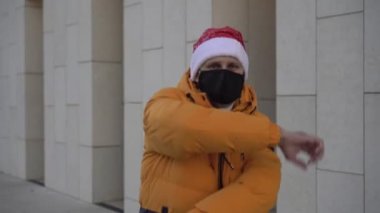 Noel, koruyucu maskeli bir adam Noel Baba şapkasıyla dans ediyor.