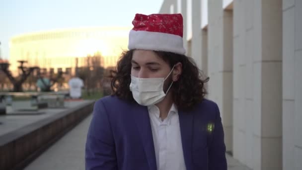 Mutlu adam tıbbi maske ve Noel Baba şapkasıyla dans ediyor. Coronavirus sırasında yeni yıl ya da Noel. — Stok video