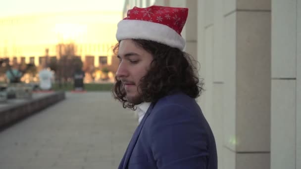 El hombre feliz en el sombrero de Papá Noel se regocija en Navidad. Un hombre de negocios está bailando en la calle en un sombrero de Año Nuevo — Vídeos de Stock