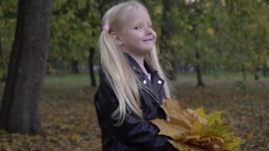 Sonbaharda parkta küçük bir kızın portresi. Sarı yapraklı bir çocuk doğada