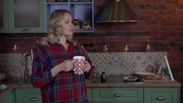 Szczęśliwa kobieta w kuchni pije kawę z kubka. Romantyczna młoda kobieta w kuchni — Wideo stockowe