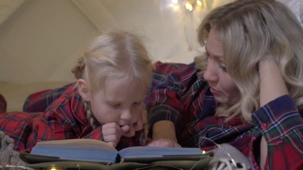 Los padres con un niño leen un cuento de hadas antes de acostarse. mamá lee un libro a su hija — Vídeo de stock