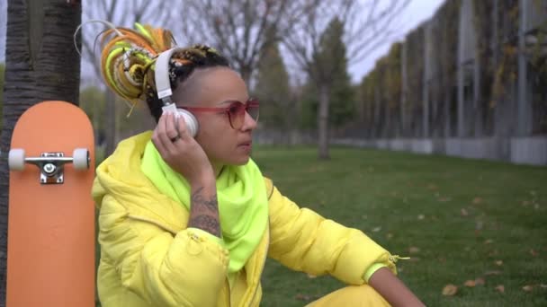 現代の若い女性は屋外でヘッドフォンで音楽を聴いています。現代の若者の生活様式 — ストック動画