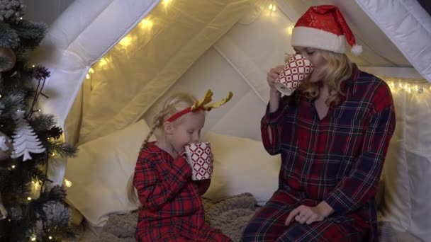 Mutter und Kind trinken zu Hause im weihnachtlichen Interieur Kakao. Menschen im Pyjama an Silvester — Stockvideo