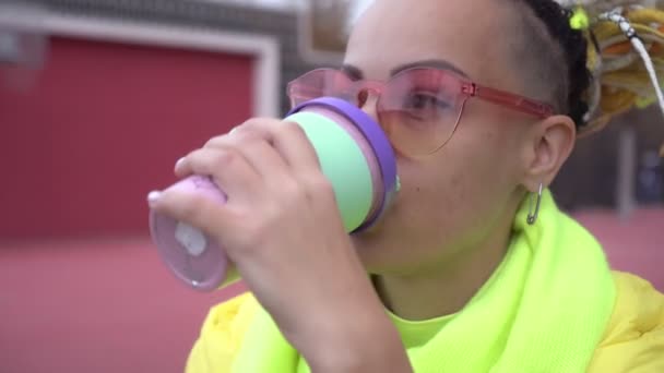 Młoda nowoczesna kobieta w okularach pije kawę ze szklanki na świeżym powietrzu. Portret kobiety jedzącej przekąskę na ulicy — Wideo stockowe