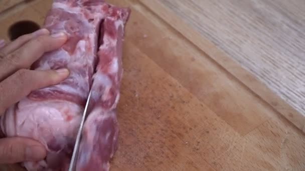 En man skär kött med kniv på en träskiva. En man styckar kött i bitar och tillagar fläskbiffar — Stockvideo