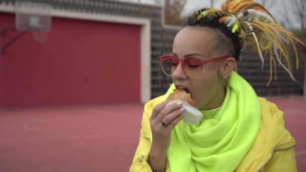 Женщина ест хот-доги за обедом на улице. Человек, который ест фаст-фуд на улице. Голодная женщина ест сэндвич в парке — стоковое видео