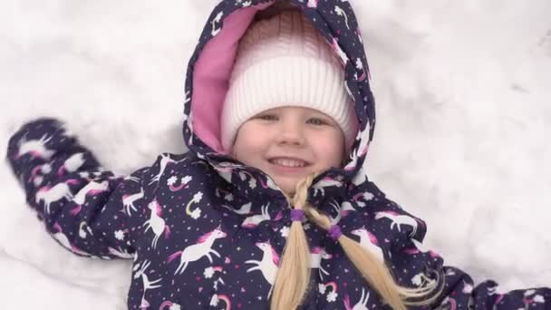 Щаслива дитина лежить на снігу. Весела дівчинка грає на снігу взимку — стокове відео