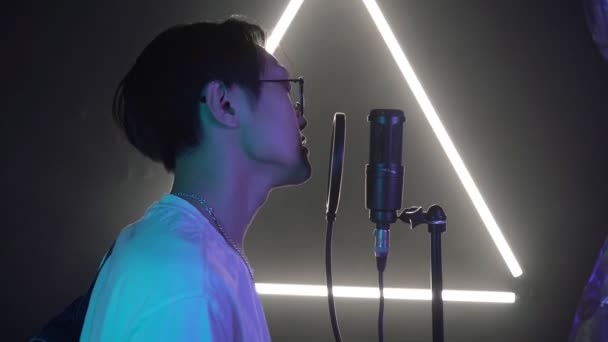 ネオンレコーディングスタジオで若い男性歌手。アジア人がマイクに歌いポップスターが歌を録音する — ストック動画