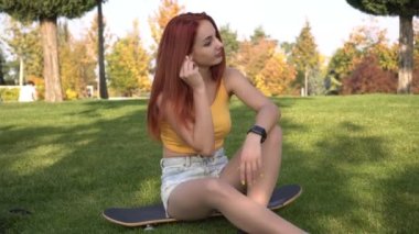 Güzel kızıl saçlı kadın dışarıda kulaklıkla müzik dinliyor. Modern genç bayan öğrencinin açık hava portresi.