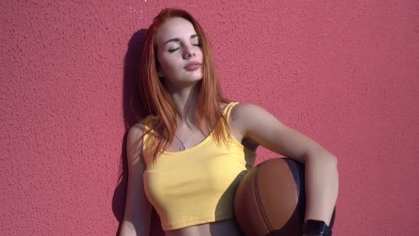 Mujer atractiva joven con una pelota de baloncesto al aire libre. Retrato de una mujer atlética en la cancha de baloncesto — Vídeo de stock