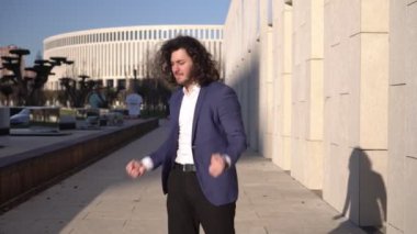 Erkek işadamı başarıya sevinir ve sokaklarda dans eder. Açık havada mutlu bir iş adamının portresi