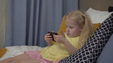 Çocuk akıllı telefondan video izliyor. Çocuk kız evde akıllı telefon kullanıyor. Modern bir çocuk cep telefonunun ekranına bakar.