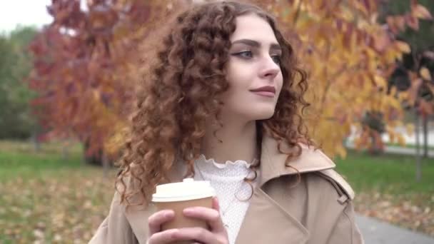 Mujer atractiva joven bebiendo café en el parque de otoño. Mujer feliz bebiendo café o té en una taza de papel — Vídeo de stock