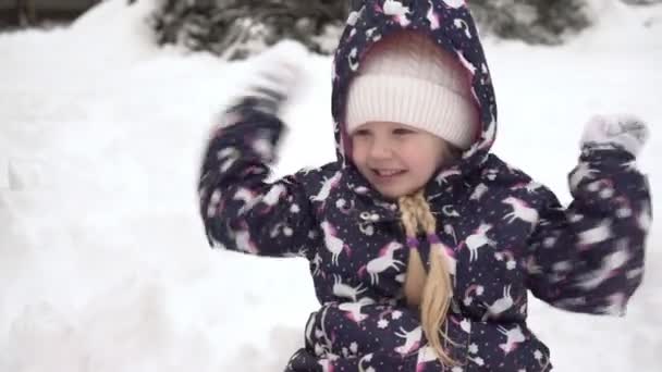 Un enfant joyeux joue et jette des boules de neige à l'extérieur. Bonne fille à l'extérieur un jour d'hiver. Enfance joyeuse en hiver — Video